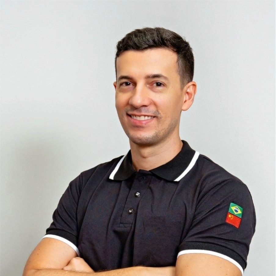Smiling person wearing a black polo shirt with crossed arms, Brazilian flag on the sleeve.