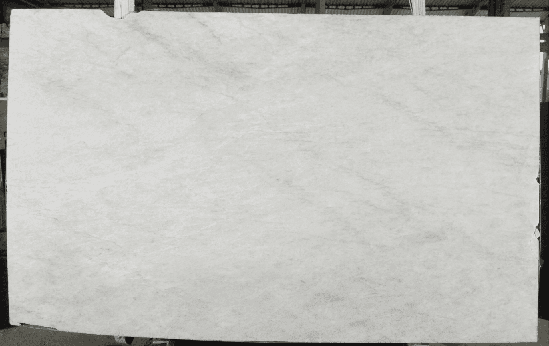 Large slab of white marble with subtle veins displayed vertically in a warehouse setting.